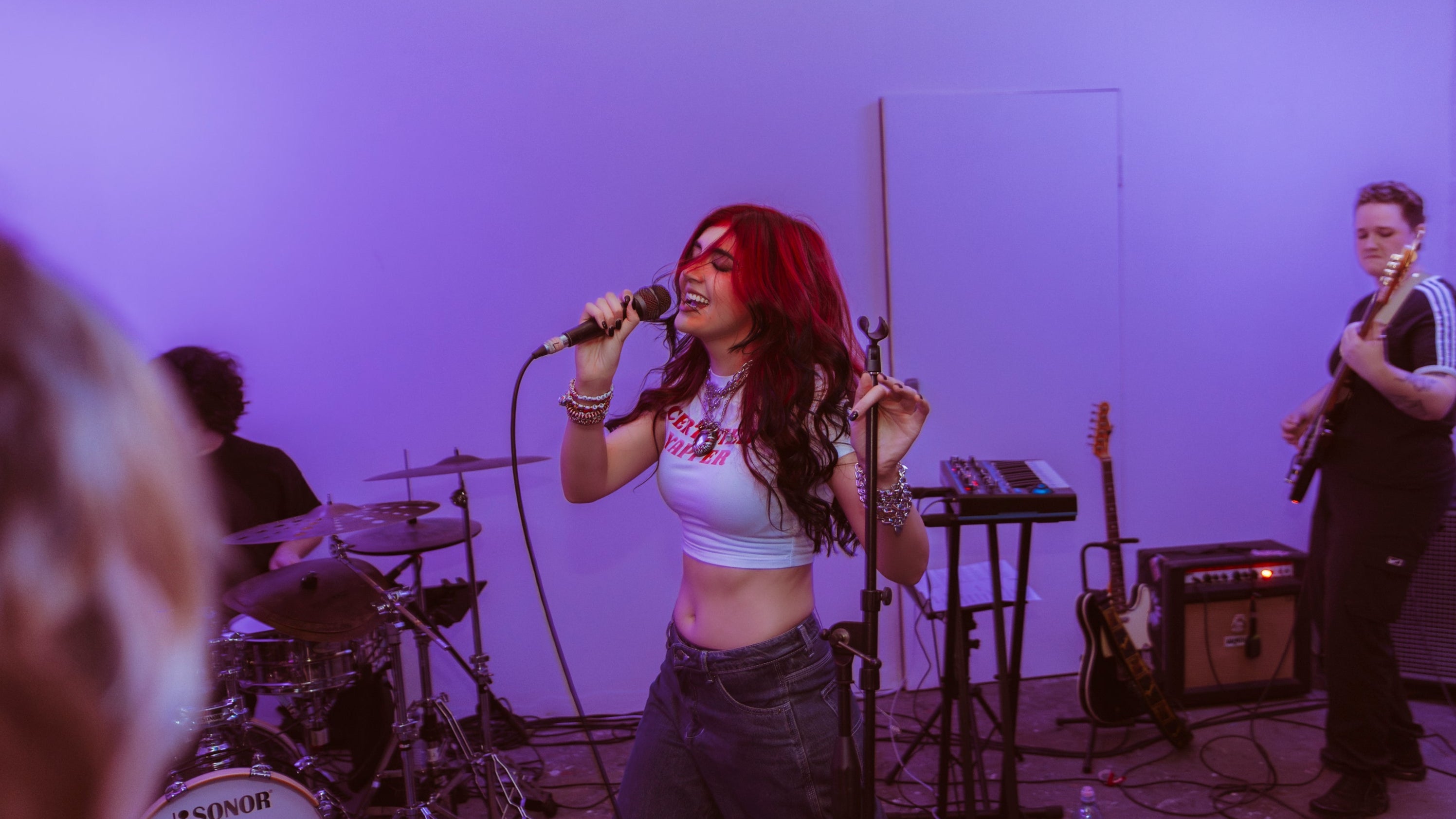Musician performing on stage with a microphone, surrounded by band equipment.